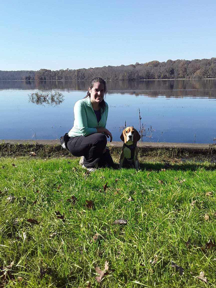 A woman kneels next to her Beagle at a lake