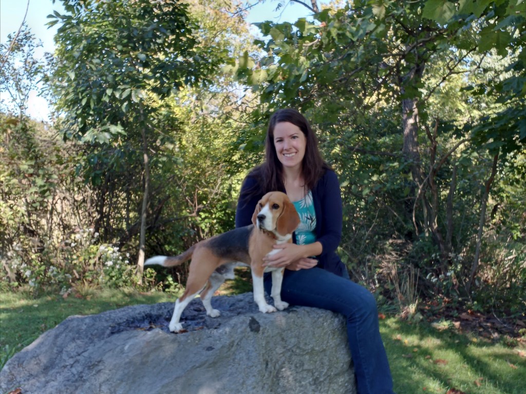 A woman sits on a rock with a Beagle by her side